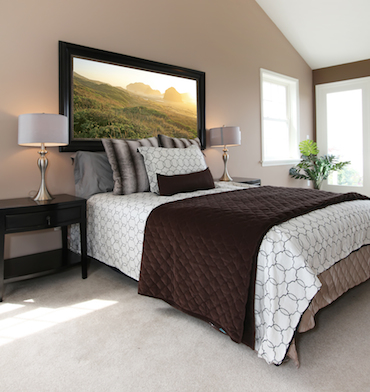 a carpeted room with a high sloping cieling, two small bright windows, and a two-person bed with a bedside table and lamp on each side