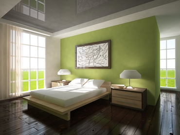room with a hardwood floor, bright windows on two sdies, anda  two-person bed with a bedside table and lamp on each side